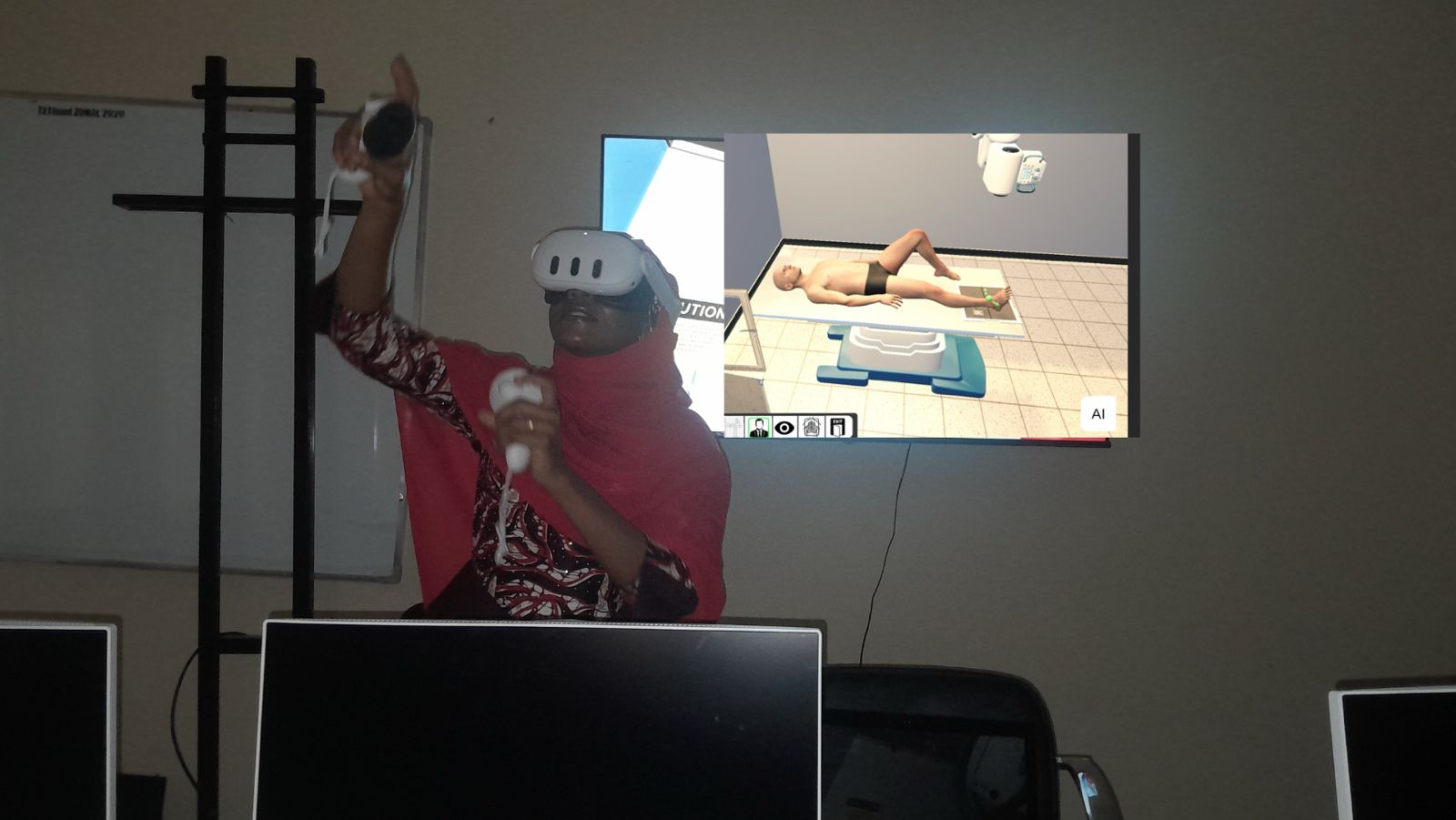 A trainee in a VR headset with the virtual X-ray room shown on a screen behind her